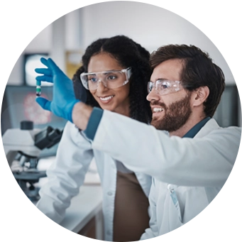 Two scientists in a laboratory, wearing safety glasses and gloves, analyzing a sample together.